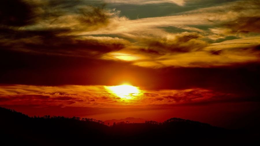 The sun sets through a dramatic display of clouds, creating a dynamic interplay of light and shadow across the landscape, possibly a breathtaking view from the resort