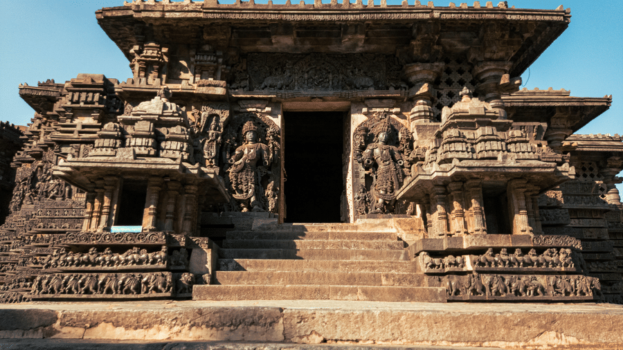 An overview to the entrance of Halebidu Temple with stone carved structures on either side of the door and steps leading to the entrance.