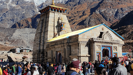 Facade of Kedarnath Temple, among the top travel destinations in Uttarakhand, against mountains and pilgrims walking up to the entrance