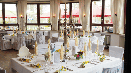 A bright banquet room featuring a large rectangular table decorated with tall candelabras and yellow floral accents.