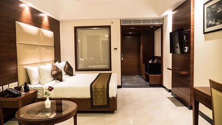 Side angle view of a Premium Room showcasing a bed, tea table, flat-screen TV, wall frame, and warm lighting.