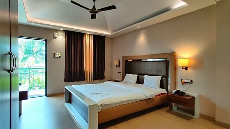 Overview of a Super Premium Room at The Kanila Resort with a queen sized bed, a nightstand, a TV, and a desk. 