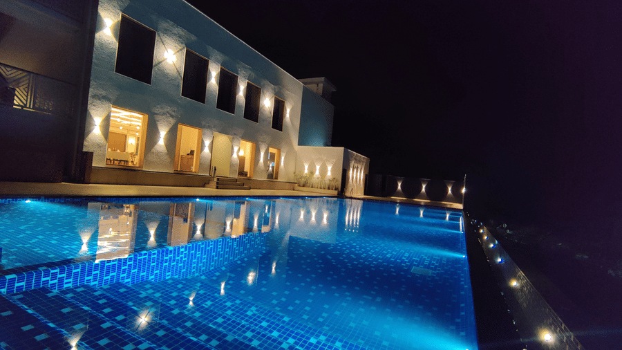 An illuminated outdoor swimming pool and modern main building at Bindiga Peak Resort lit up at night.