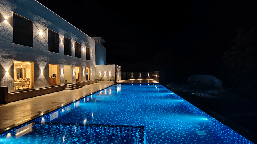 A long, brightly lit blue swimming pool running alongside the building at Bindiga Peak Resort at night.