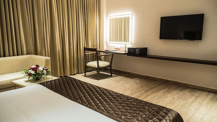 A king size bed placed in front of the desk and TV of Premium Room at Grand Ashok, Thanjavur.