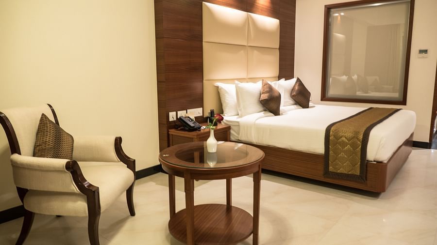 view of a king size bed and a small table with chair of a Premium Suite Room of MM Legacy, Kanchipuram