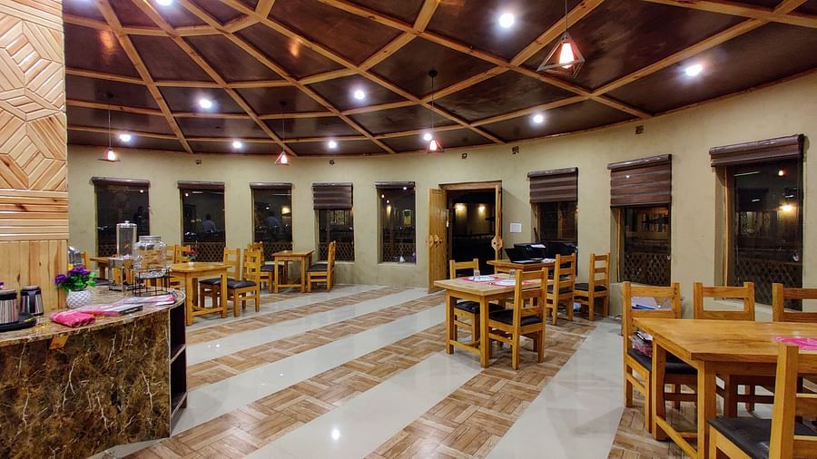 The interior of a dining area at White Sands Resort, Ladakh, with wooden tables and chairs, a buffet setup in the background, and decorative lighting fixtures.