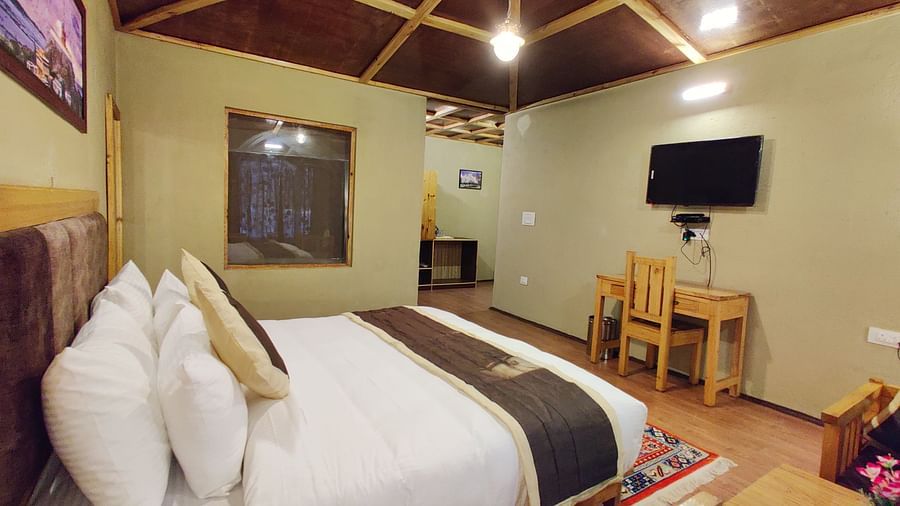 A close-up of a king size bed in Premium Cottage at White Sands Resort, Ladakh, highlighting the headboard, pillows, and bedside table.