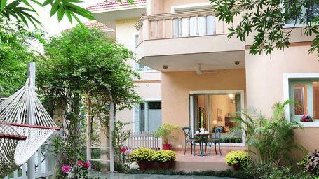 Facade of Karma Chalets, our luxury hotel in Delhi NCR, with a garden and paved path.