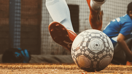 A worn soccer ball rests on the ground, with a foot visible, suggesting a game or practice at Nirantara Resort & Spa.