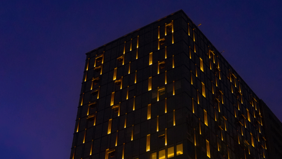 A vertical shot of the tall hotel building with glowing signage under a dark blue sky - Praveg's Grand Eulogia, Ahmedabad