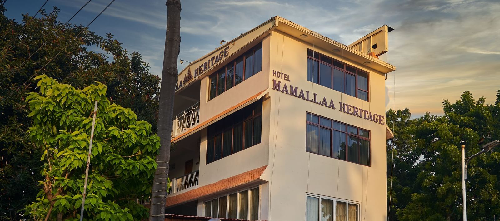 The exterior of Hotel Mamallaa Heritage from a slightly different angle, showcasing its multi-story structure and architectural details under a pleasant sky.