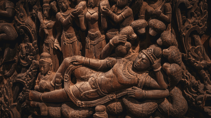 Intricate stone carving depicting the Hindu god Vishnu reclining, surrounded by other figures
