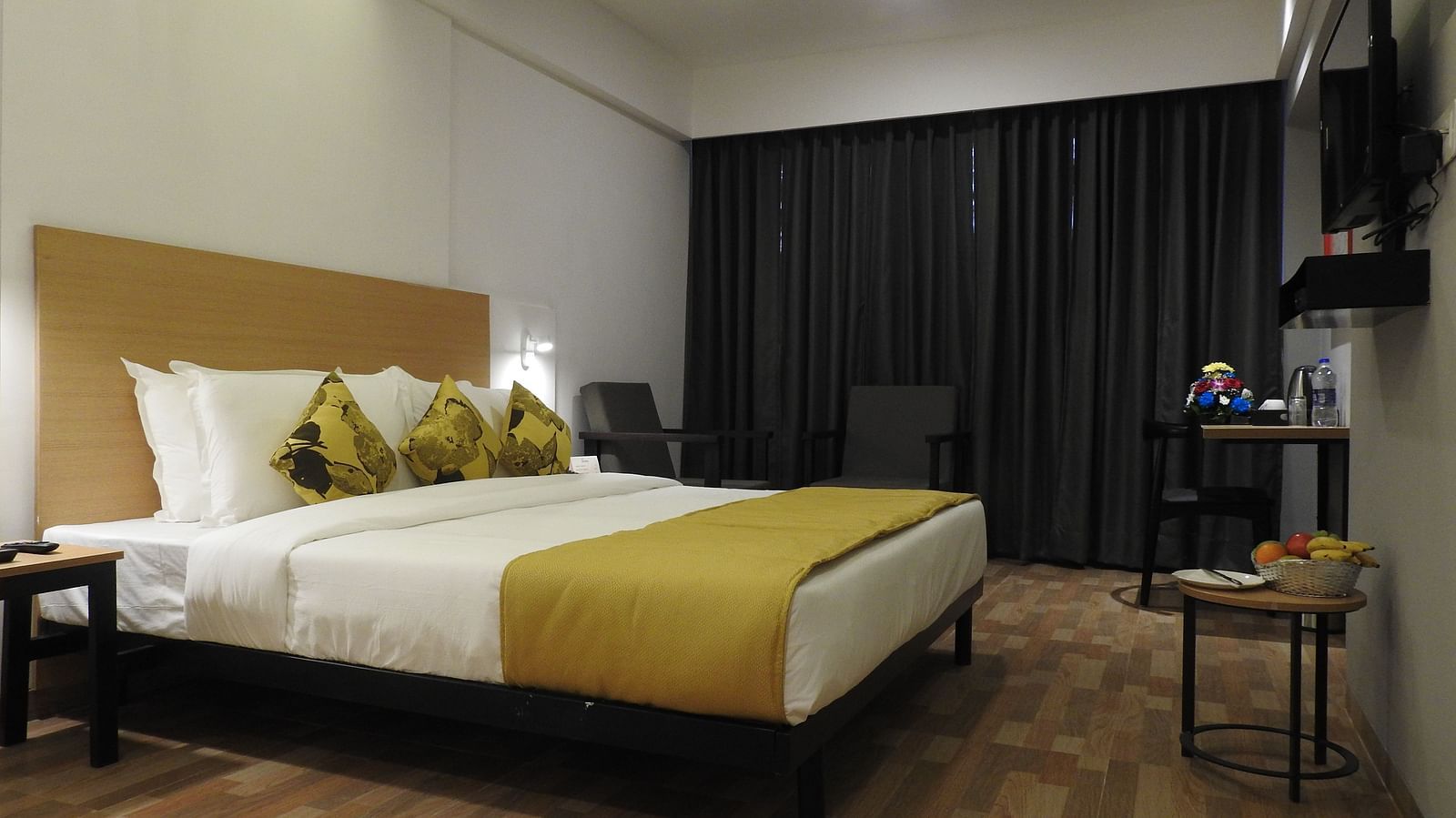 Another view of the hotel room with a double bed, gold and white bedding, a wooden headboard and a television - TGI Ameya Grand, Goa