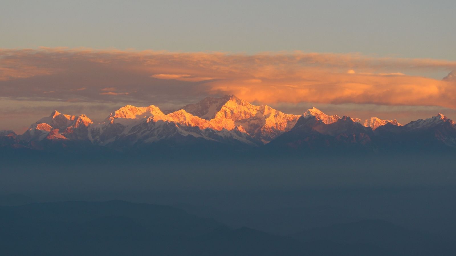 A far shot of mountains with a backdrop of peachy hues of the sky