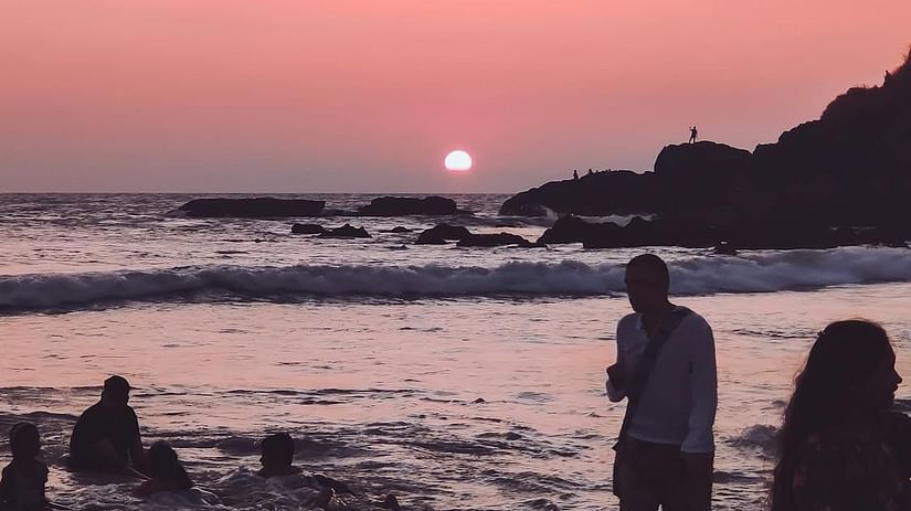 Silhouetted figures on a sandy beach at sunset, with gentle waves meeting the shore under a soft sky.