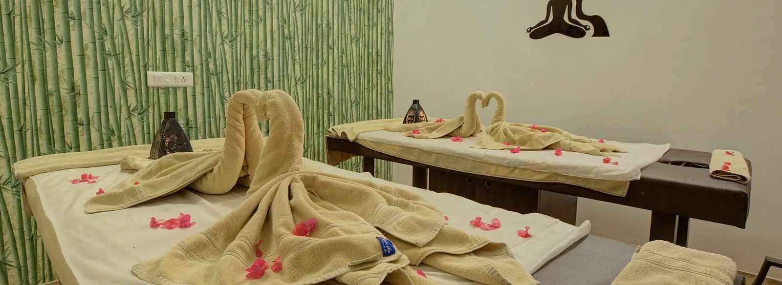 Cosy spa room with two massage tables, folded towels, rose petals, and a bamboo-themed wall. - Bamboo Saa, Udaipur