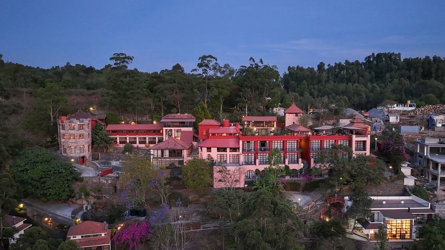 Aerial view of a red-roofed resort nestled in a lush, forested mountainous area at dusk.  | Mango Hill, Yercaud