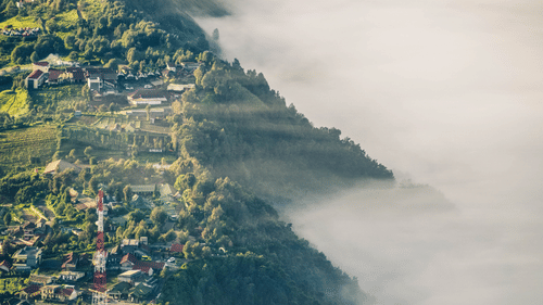 A high-angle view of a village or town nestled in a valley, partially obscured by clouds.