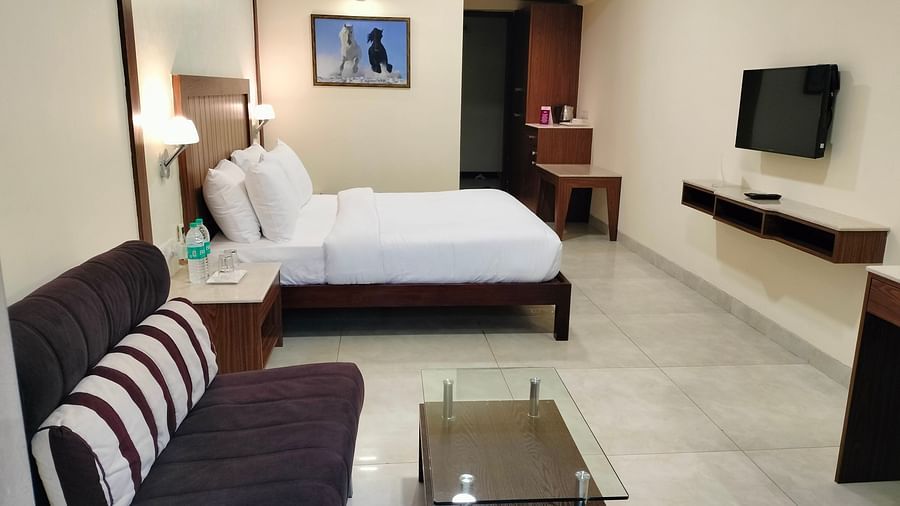 An mage of a bedroom with a double size bed, a sofa with glass table, a flat TV screen, and a tea table - VITS Lonavla