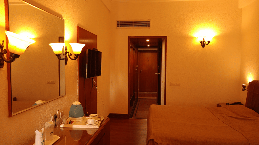 Room interior at Hotel Gold, Panipat with a bed, lamps, desk, and a mirror near the entrance.