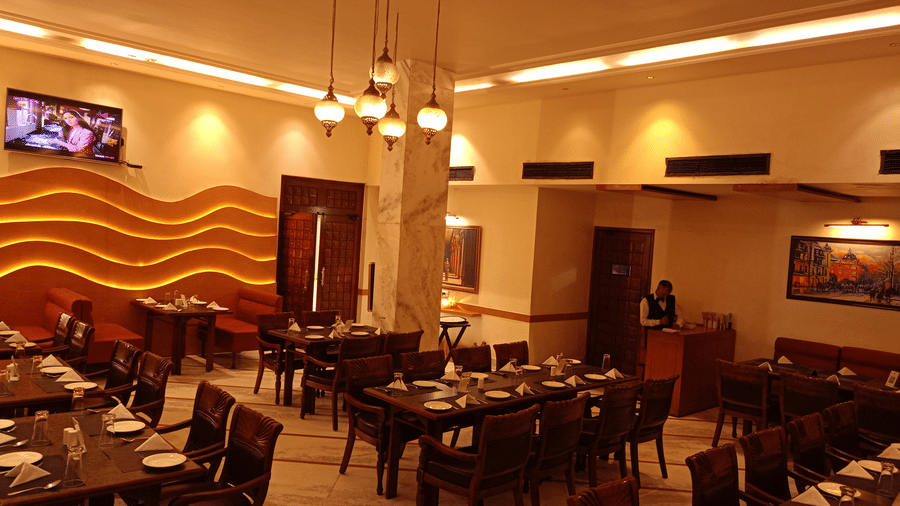 Dining area at Hotel Gold, Panipat featuring set tables, chairs, and a wavy patterned wall design.