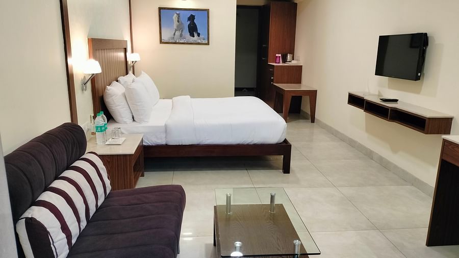 An mage of a bedroom with a double size bed, a sofa with glass table, a flat TV screen, and a tea table - VITS Lonavla