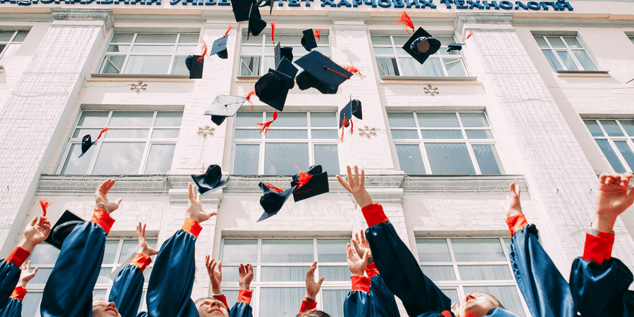Students in gowns tossing their graduation caps in front of a university building