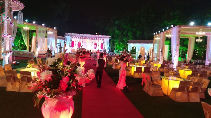 A vibrant outdoor wedding reception is decorated with pink and white flowers and bright lights, with a red carpet leading through the centre - Clarks Avadh, Lucknow