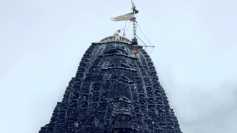 A tall stone temple tower viewed from below with a flag at the top against the sky.