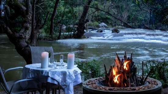 Outdoor candlelit dinner setup by a river in the evening- Amanvana Resort And Spa, Dining in Coorg
