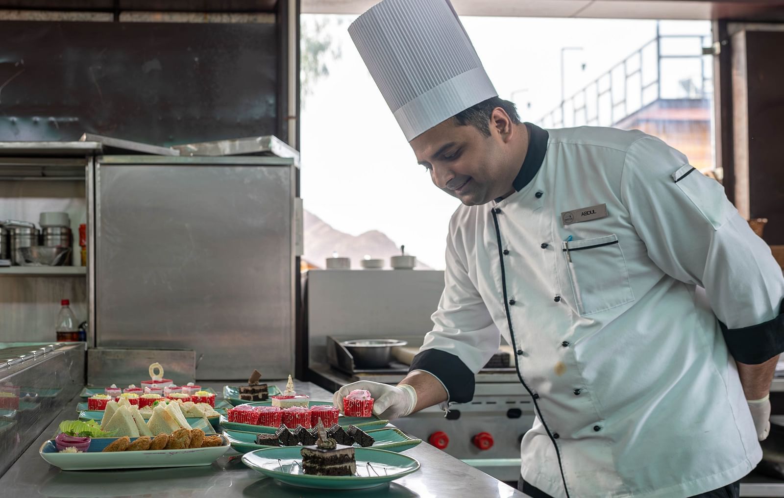 A chef in a white uniform and a tall chef's hat working in a kitchen.