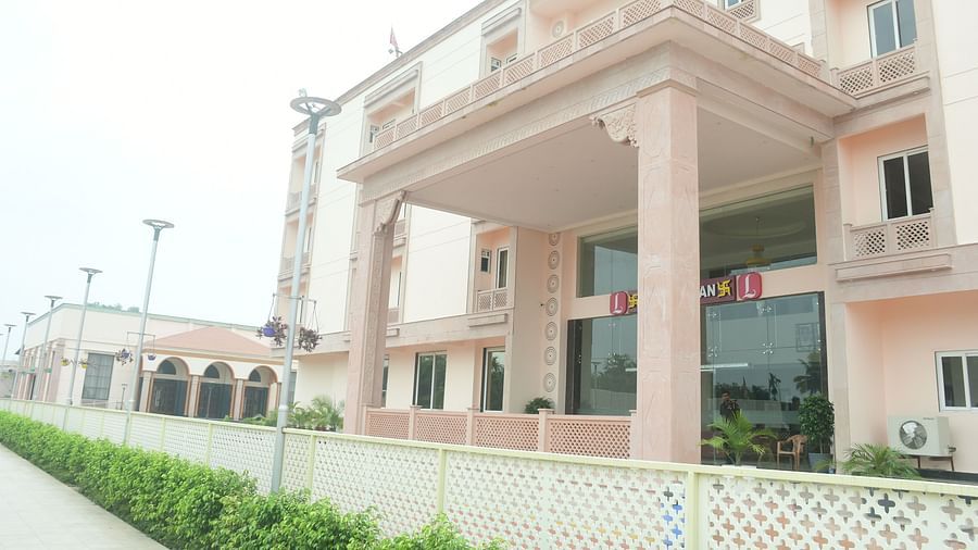 A light-pink building with balconies and a covered walkway is seen under a bright sky - Kankidham Lords Inn
