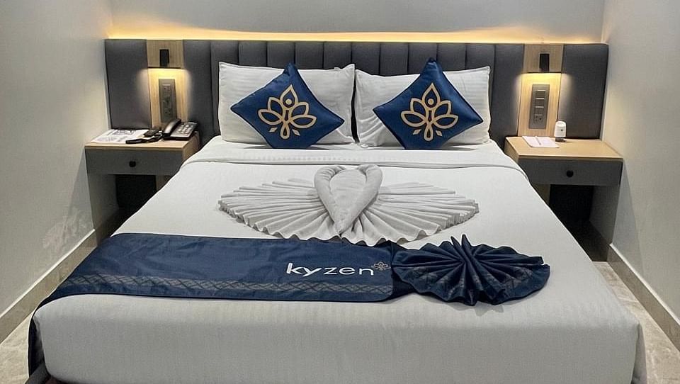 Bed with decorative cushions, side tables, and soft lighting, featuring towel art in the shape of a heart at Hotel Kyzen HiTech City – Your Zenly Stay