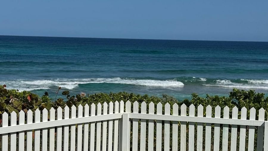 The ocean with small waves is visible beyond a well-maintained lawn enclosed by a picket fence. The sky is a clear | Abaco Inn
