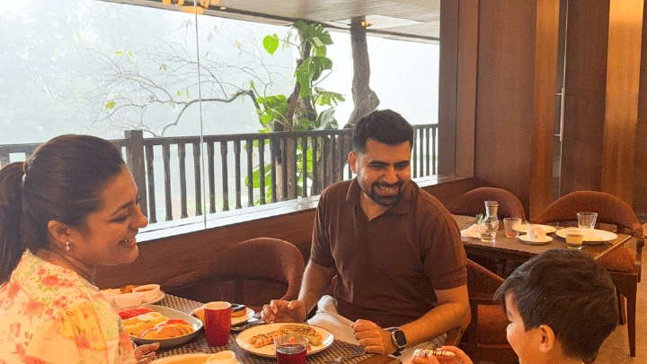 A family of three enjoying a meal together at an indoor restaurant table with a balcony view of greenery.
