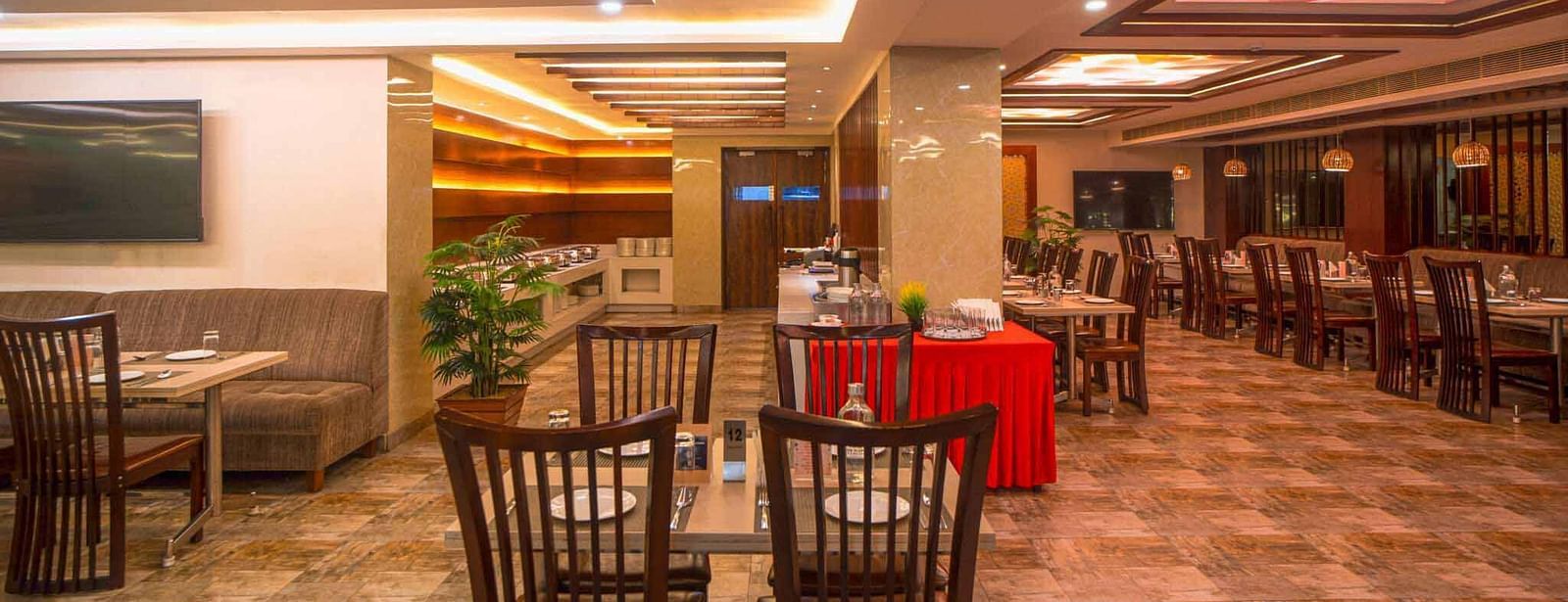 A modern dining room at Mansha Hotel Regency with warm lighting, wooden tables and chairs, and a television screen on the wall.