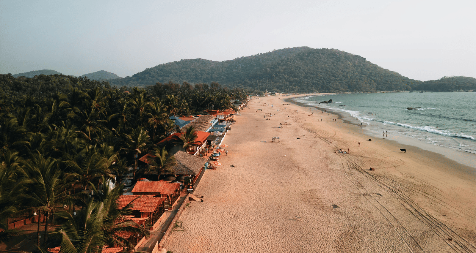 An aerial view of a wide, sandy beach featuring row of buildings and trees lining the shore.