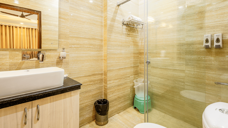 Spacious hotel bathroom with a glass shower enclosure, wash basin, and premium amenities.