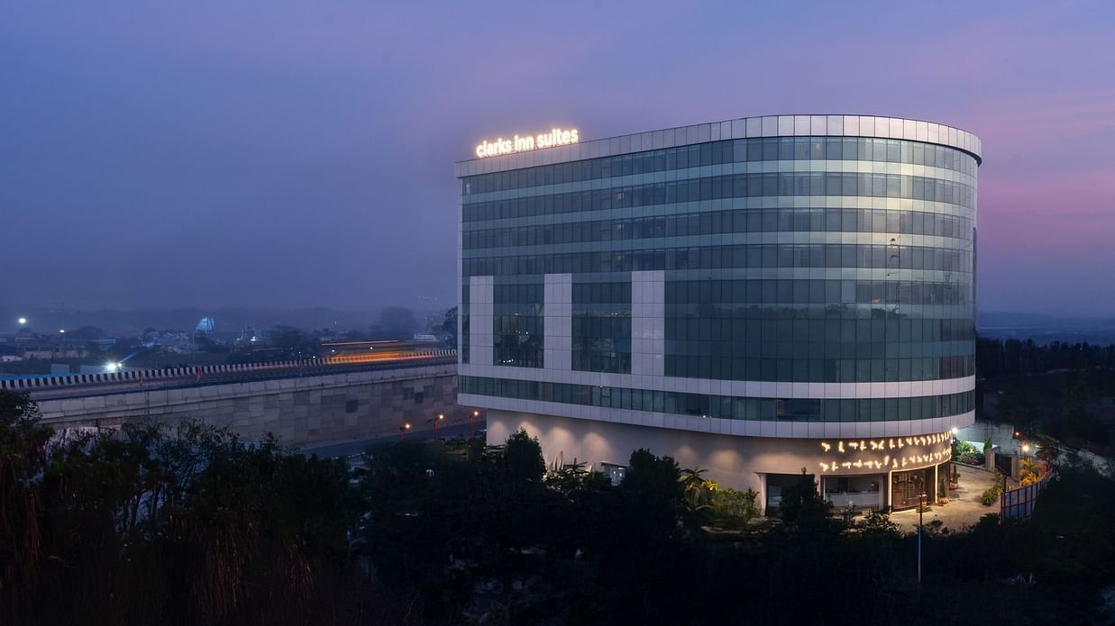 Evening shot of a curved glass hotel building with illuminated signage against a dusky sky at Clarks Inn Suites, Hyderabad