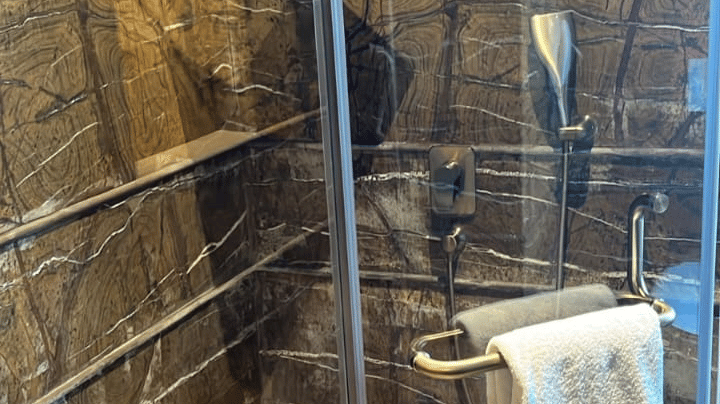 A spacious shower area with stone tiling and a glass partition at Aamaghati Wildlife Resort.