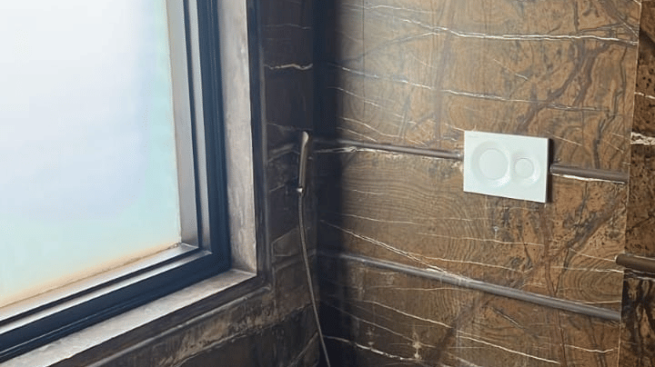 A clean toilet area with natural stone walls and a small window at Aamaghati Wildlife Resort.