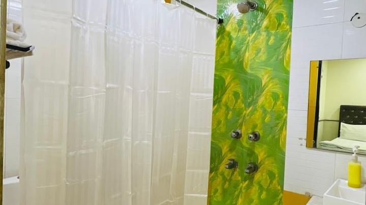 A brightly lit bathroom with a shower curtain and light green accents, ensuring a refreshing experience for guests. | Family Room | Ajay Guest House