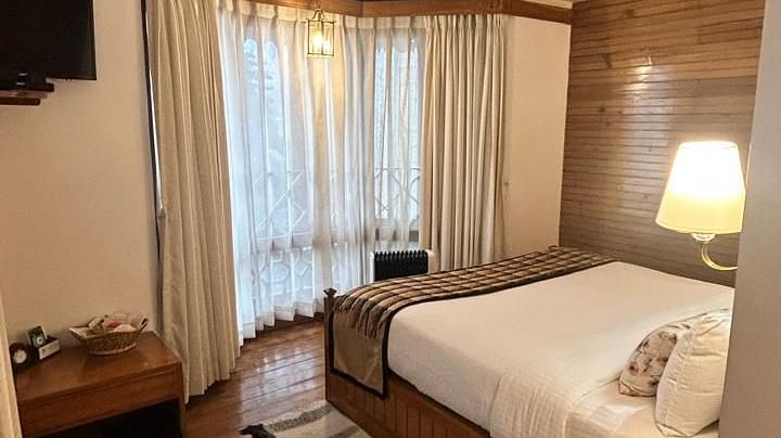 A portrait view of the Executive Suite featuring a double bed facing a curtained glass window and a TV in the Cedar Inn in Darjeeling.
