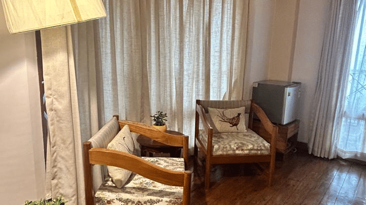 Living area of the Executive Suite at Cedar Inn with wooden flooring, seating arrangement, a table lamp, and large windows bringing in natural light.