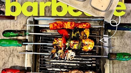 A close-up of a barbecue grill plate at Themis Barbecue House, Ambala, featuring colorful skewers and dipping sauces.