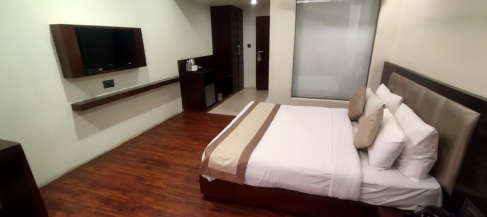 A hotel room with a large bed, warm lighting, wooden floors and a seating area - TGI Apple Inn, Jaipur 