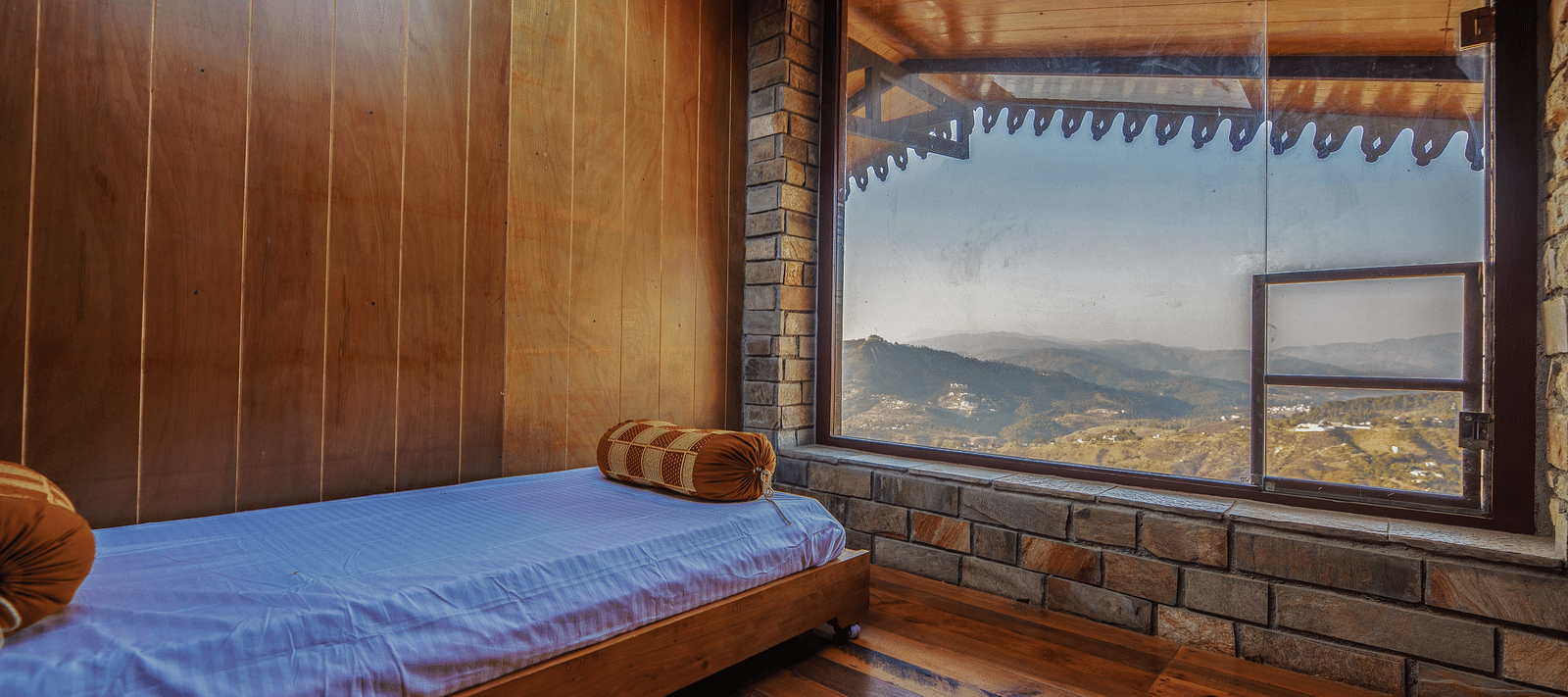 A cosy room with wooden walls, a single bed, and a large window showcasing mountain views. - Blusalzz Homes The Himalayan Bungalow, Almora
