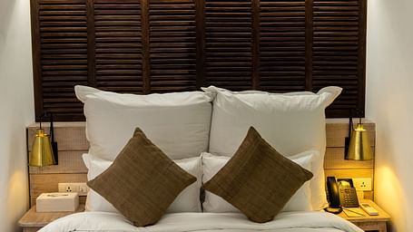A room with a bed, pillows and cushions and bed side tables with lamps on either side - The Nanee