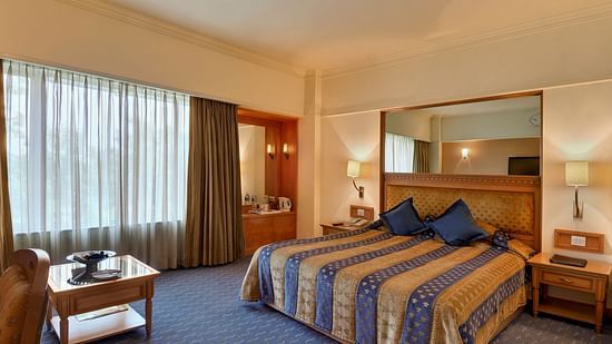 Superior Room at Pride Hotel Pune featuring a plush bed with a large rectangular mirror over the headboard and a window next to it